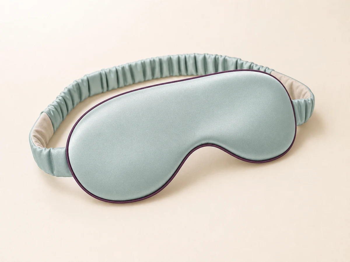 Seafoam satin contoured sleep mask with deep plum piping and a covered gathered elastic strap